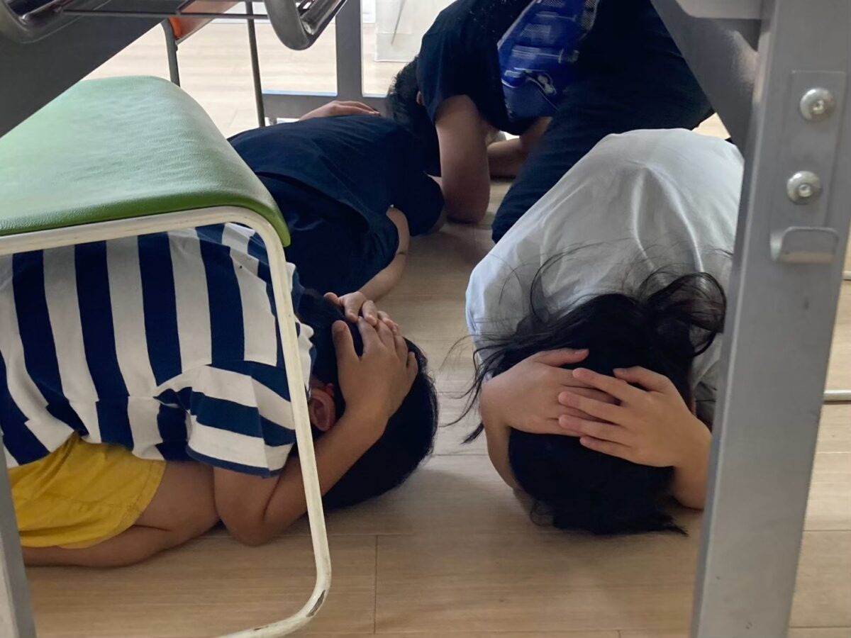 学童の防災学習で机の下にもぐり頭を守る練習をする子どもたち