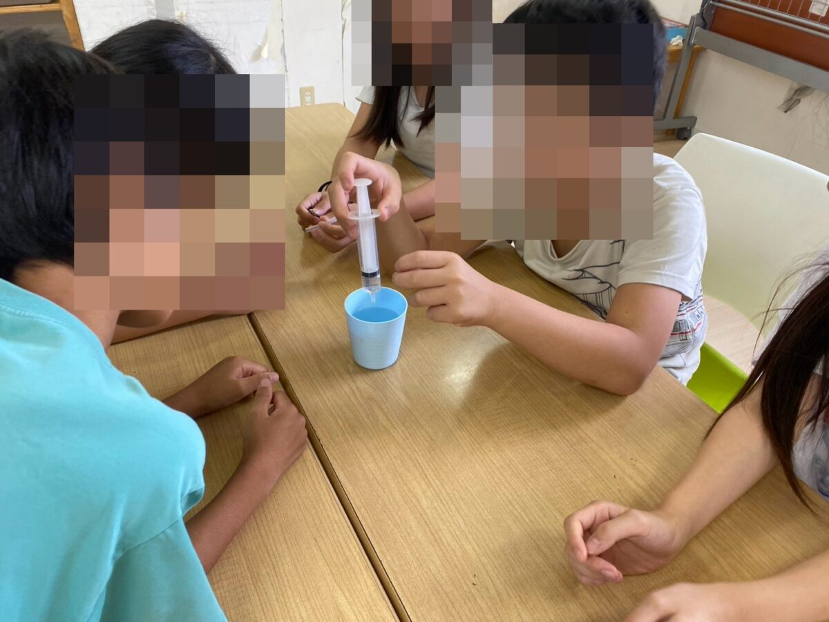 学童の理科実験教室で注射器と色水を使って実験する小学生